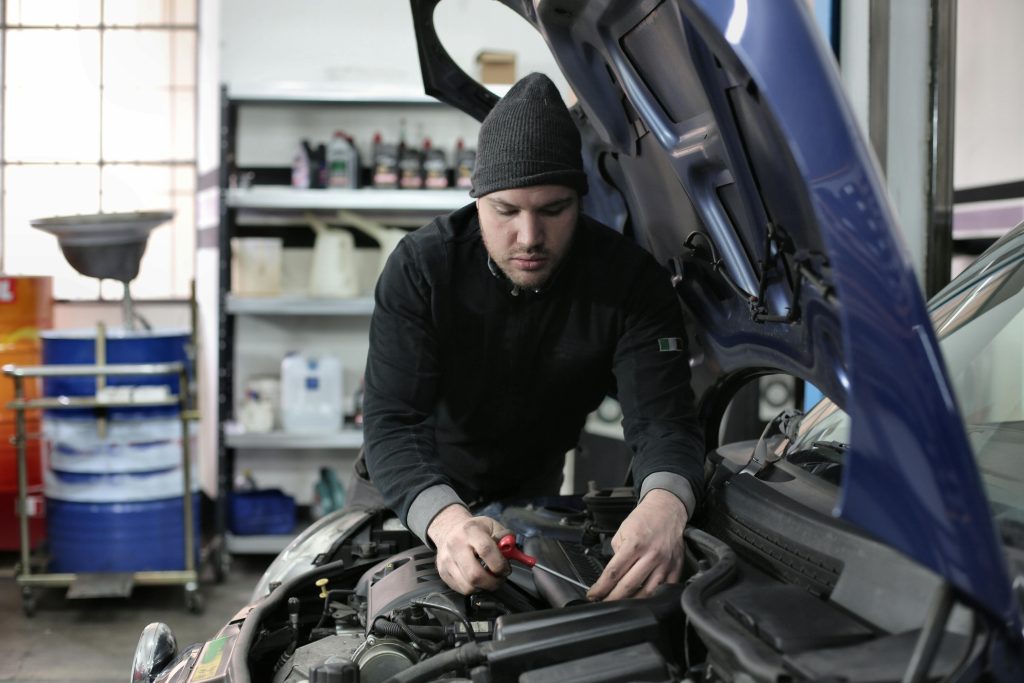pexels-photo-3807329-3807329 Man working under car hood in a garage, focused on engine repair